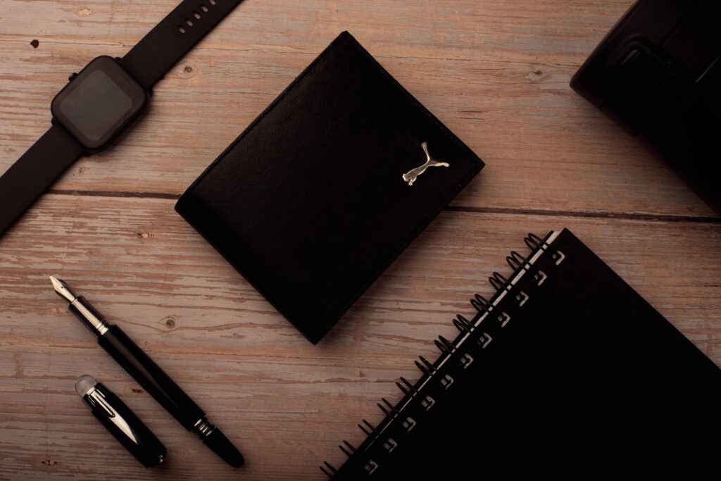 A stylish flat lay of desk accessories featuring a wallet, watch, fountain pen, and spiral notebook.